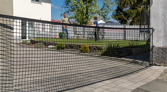 Absperrnetz zwischn Mauer un Wand vor Hofeinfahrt, mit 2 Leuten spielend imm Garten